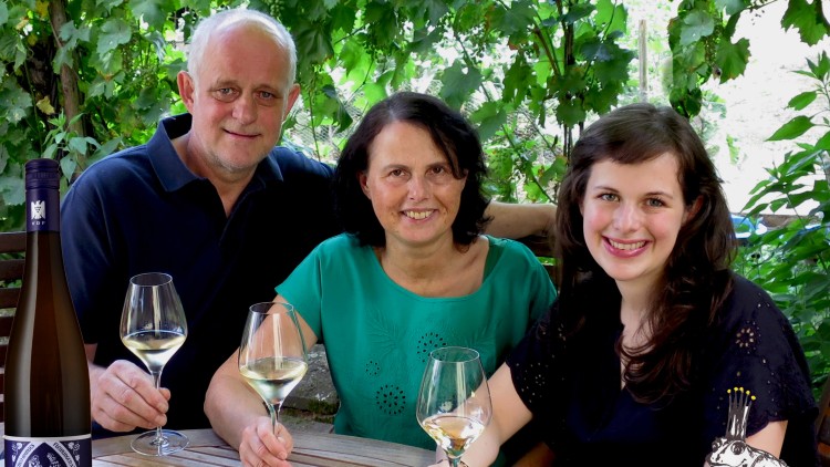 Drei Personen halten Weingläser in der Hand, im Vordergrund steht eine Flasche Riesling und Aprikosen liegen auf einem Holztisch.