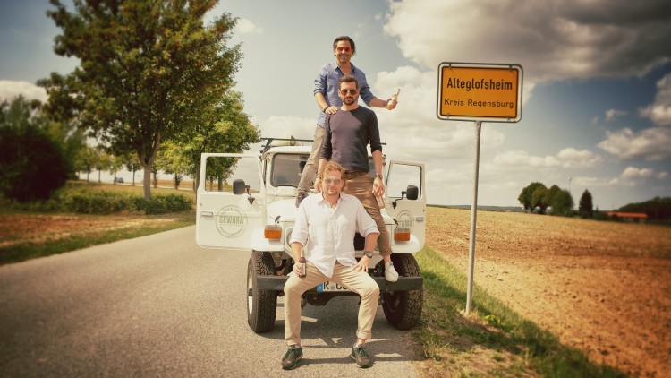 Weißer Geländewagen mit offenstehenden Türen auf Landstraße, Ortsschild „Alteglofsheim, Kreis Regensburg“ und Baum im Hintergrund.