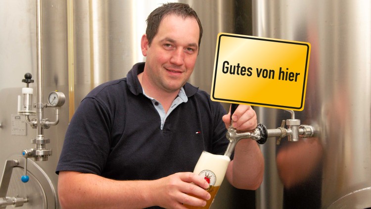 Person füllt ein Glas Bier an einem Metallzapfhahn, gelbes Schild mit der Aufschrift Gutes von hier im Vordergrund.