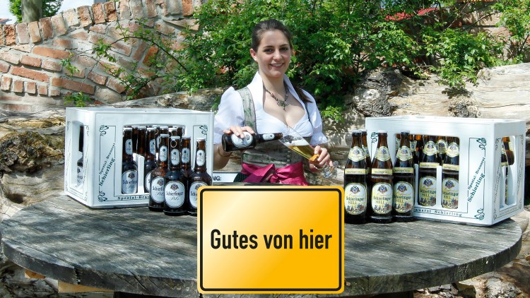 Eine Person schenkt Bier in ein Glas, umgeben von Bierflaschen und Bierkisten, Schild mit Text: Gutes von hier.