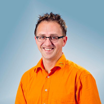 Person mit kurz geschnittenem, dunklem Haar trägt ein orangefarbenes Hemd mit GLOBUS-Logo vor einem blauen Hintergrund.