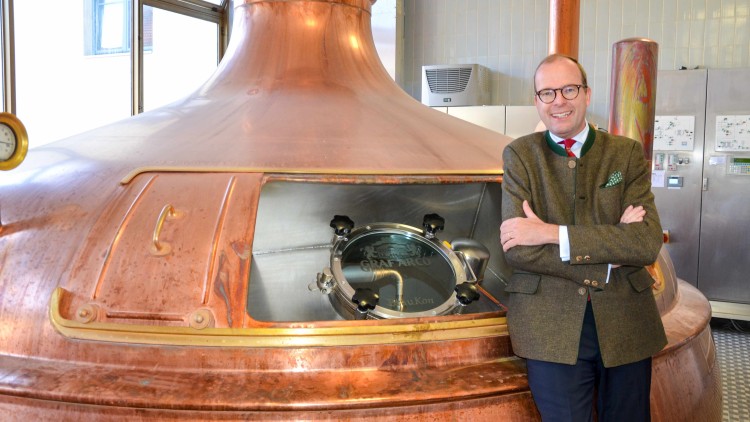 Eine große Kupferbrauanlage mit einem geschlossenen Glasdeckel und Gravur „GRAF ARCO“ steht in einer hellen Industriehalle.