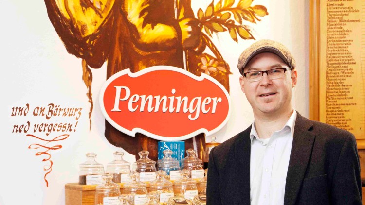Mann hält links ein Glas mit Wurzeln und rechts eine Flasche „Penninger Blutwurz“, Hintergrund mit „Penninger“-Logo.