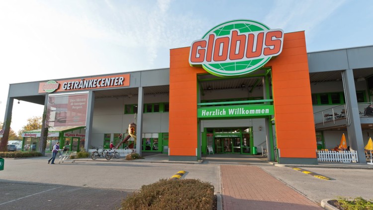 GLOBUS Getränkecenter mit großem grünen Schriftzug „Herzlich Willkommen“, Eingangstür und mehreren Personen auf dem Parkplatz.