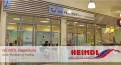 Eine Filiale von HEINDL Reisebüro mit Glasfassade, innen TUI-Werbung, Sitzbereich und Plakate, außen das HEINDL-Logo.