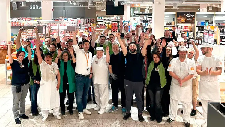 Eine Gruppe von Mitarbeiterinnen und Mitarbeitern steht in einem GLOBUS Markt und hält lachend die Arme in die Höhe.