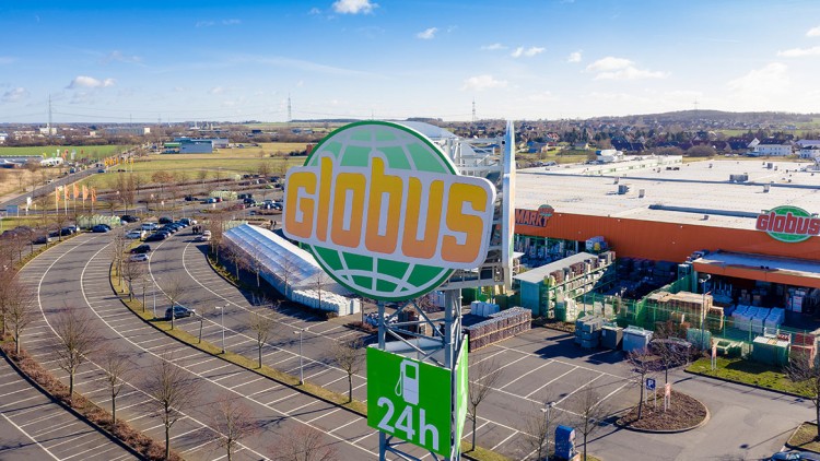 Großes GLOBUS-Logo auf einem Turm mit „24h“-Tankstellenschild, im Hintergrund ein GLOBUS Warenhaus und Parkplätze.