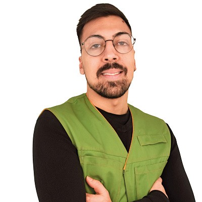 Person in schwarzem Oberteil trägt eine grüne Weste mit Reißverschluss und gekreuzten Armen.