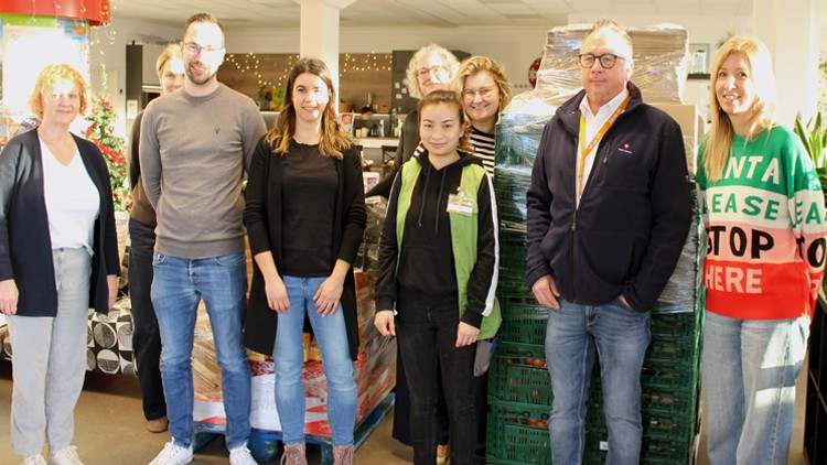 Mehrere Personen stehen in einem geschmückten Verkaufsbereich neben gestapelten Gemüsesteigen und Weihnachtsdekorationen.