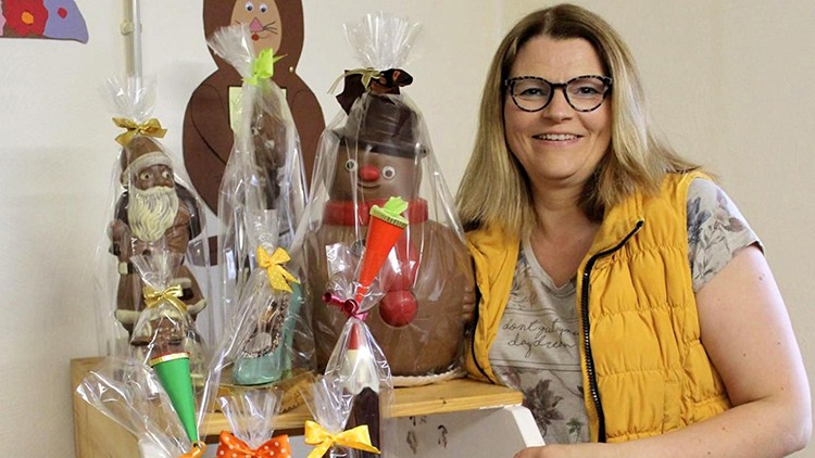 Verschiedene Schokoladenfiguren und Geschenke mit bunter Verpackung und Schleifen auf einem hölzernen Regal.
