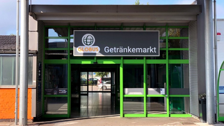Eingangsbereich eines GLOBUS Getränkemarkts mit grünem Rahmen, Glastüren und einem Schild mit Logo und Schriftzug „Getränkemarkt“.