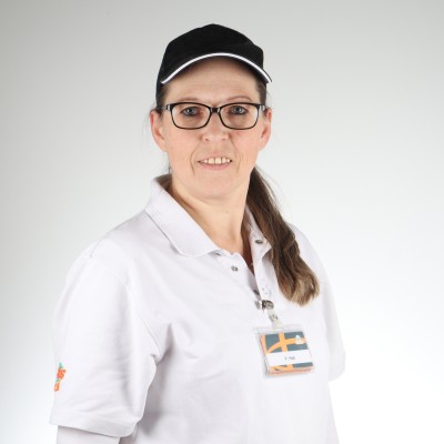 Person trägt eine weiße Polo-Arbeitskleidung mit einem Namensschild und schwarzer Schirmmütze vor neutralem Hintergrund.