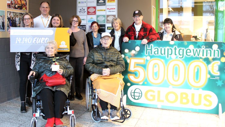 Eine Gruppe von Menschen steht vor Schildern mit den Aufschriften „14.140 EURO“ und „Hauptgewinn 5000€ GLOBUS“.