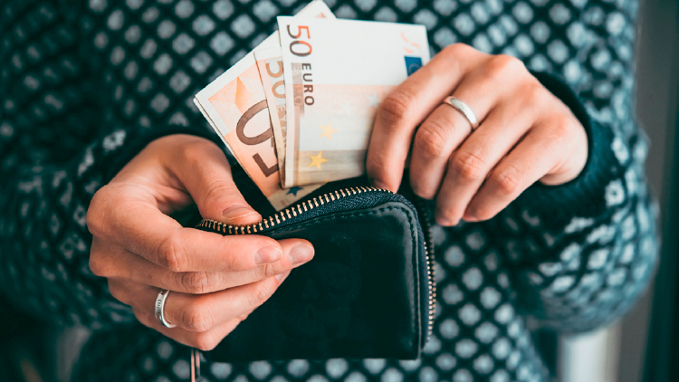 Hände halten eine geöffnete schwarze Geldbörse, aus der zwei Geldscheine im Wert von 50 und 20 Euro herausschauen.