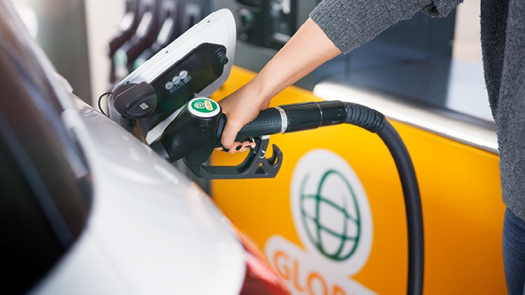 Hand tankt ein weißes Auto an einer Zapfsäule, im Hintergrund ist das GLOBUS-Logo auf einer gelben Fläche zu sehen.