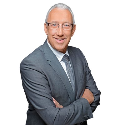 Person in grauem Anzug mit gestreifter Krawatte steht vor weißem Hintergrund und hat die Arme vor der Brust verschränkt.