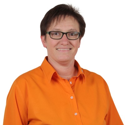 Person in orangefarbener Bluse mit weißer Knopfleiste vor weißem Hintergrund.