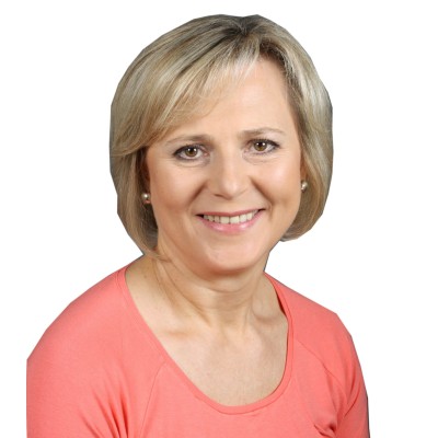 Person mit blondem, schulterlangem Haar trägt ein lachsfarbenes Oberteil vor weißem Hintergrund.