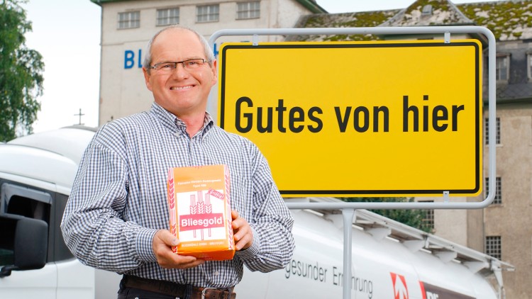 Person hält eine Packung Bliesgold vor einem gelben Schild mit schwarzem Text \