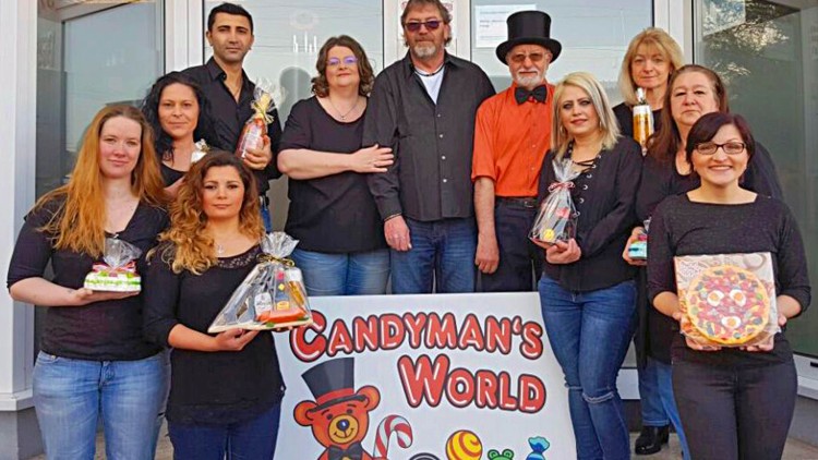 Personengruppe in schwarzer Kleidung hält Süßigkeiten und steht hinter einem Schild mit der Aufschrift „Candyman's World“.