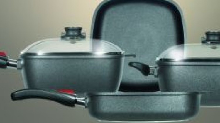 Ein Set aus Pfannen und Töpfen mit schwarzem Griff, zwei davon mit Glasdeckeln, vor einem neutralen Hintergrund.