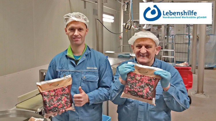Zwei Personen in blauer Arbeitskleidung halten Tüten mit Beerenmischung von „Paulus Genussmanufaktur“ in einer Produktionshalle.