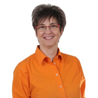Person mit kurzem dunklem Haar trägt ein orangefarbenes Hemd vor weißem Hintergrund.