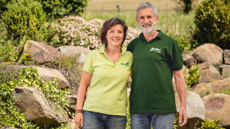 Zwei Personen in grünen Polohemden mit „Martinhof“ und „BioBau“ stehen vor einer Steinmauer mit Pflanzen.