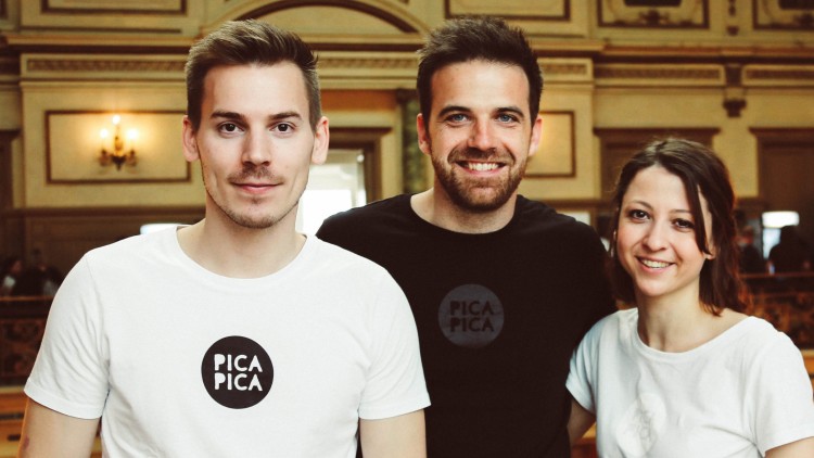 Drei Personen in einem historischen Raum tragen T-Shirts mit kreisförmigem Logo und der Aufschrift „PICA PICA“.