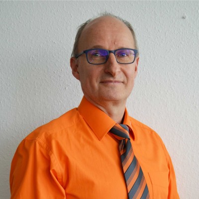 Person in orangefarbenem Hemd mit kurzärmeliger Passform und gestreifter Krawatte in Orange und Grau vor weißer Wand.
