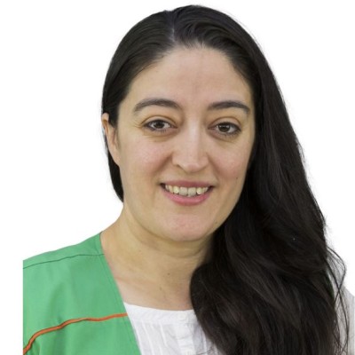 Person mit langen dunklen Haaren trägt eine grüne Weste mit orangen Details über einer weißen Bluse.