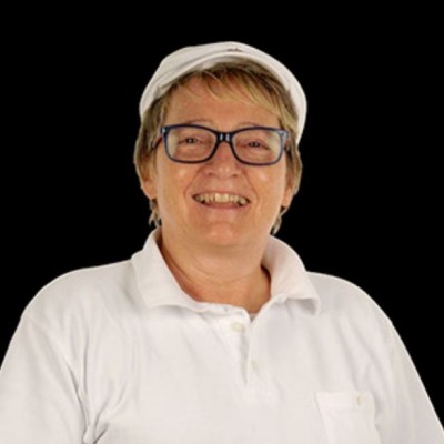 Person in weißem Polohemd mit Brusttasche und weißer Kopfbedeckung, schwarzer Hintergrund.