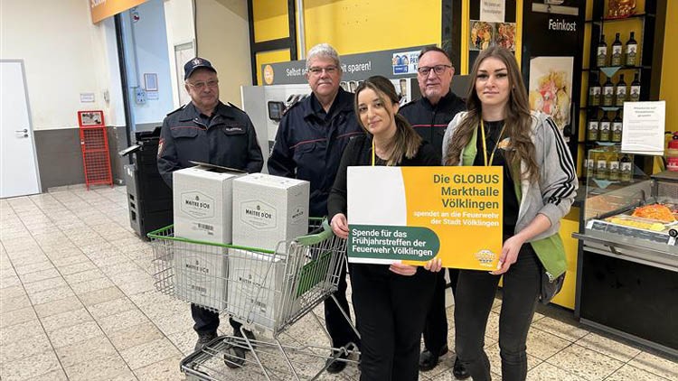 Personen stehen neben einem Einkaufswagen mit Getränkekartons, zwei halten ein Schild mit „Die GLOBUS Markthalle Völklingen“.