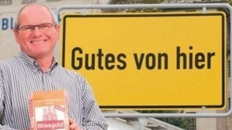 Person hält eine Packung „Bliesmühle Bliesgold“ vor einem gelben Schild mit der Aufschrift Gutes von hier.