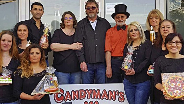 Personen in schwarzer Kleidung halten bunte verpackte Süßigkeiten vor einem Schild mit der Aufschrift „Candyman's World“.