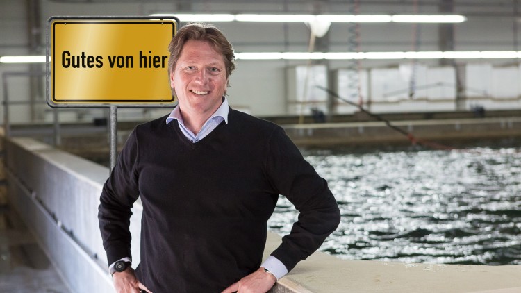 Person in schwarzem Pullover lehnt an einer Betonbrüstung, rechts Wasser, links ein gelbes Schild mit der Aufschrift Gutes von hier.