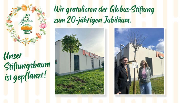 Auf einer Wiese vor einem GLOBUS Gebäude steht der Stiftungsbaum, daneben eine Frau und ein Mann neben einem Schild.