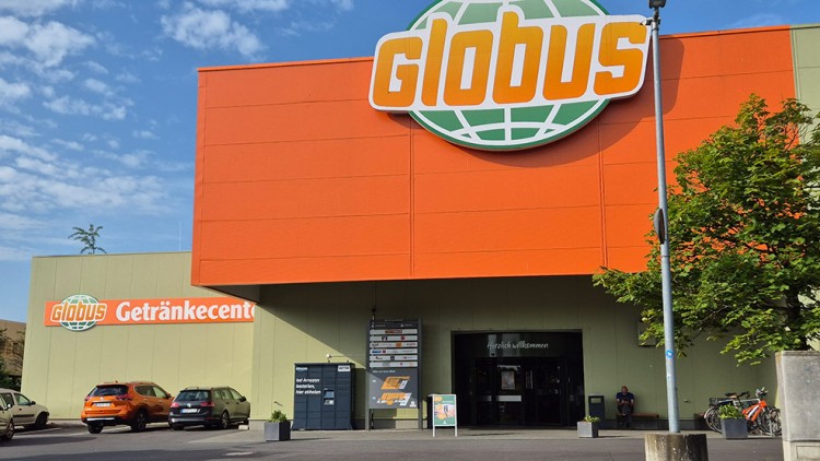 Große orange-grüne Fassade des GLOBUS Getränkecenters mit Schriftzug und Eingangsbereich, Fahrrädern und Autos davor.