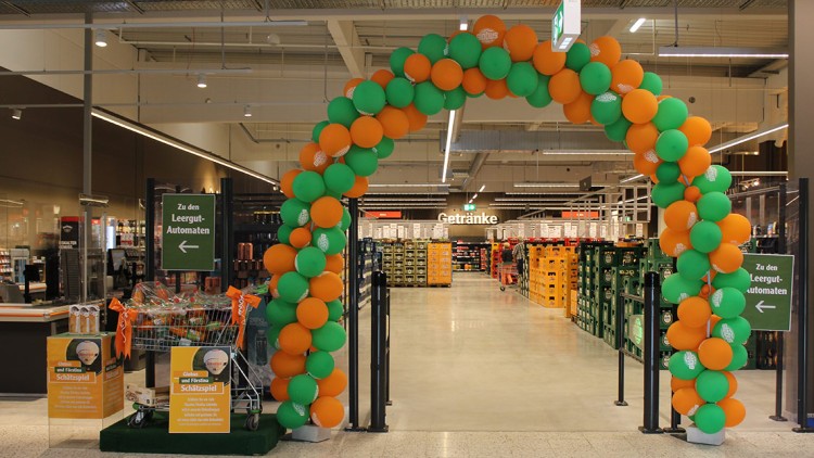 Ein bunter Torbogen aus grünen und orangefarbenen Luftballons führt in den Getränkebereich, daneben ein Hinweis zu Leergut-Automaten.
