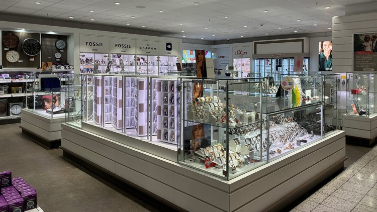 Helle Verkaufsfläche mit beleuchteten Glasvitrinen, in denen Uhren und Schmuck von Marken wie Fossil und Skagen ausgestellt sind.
