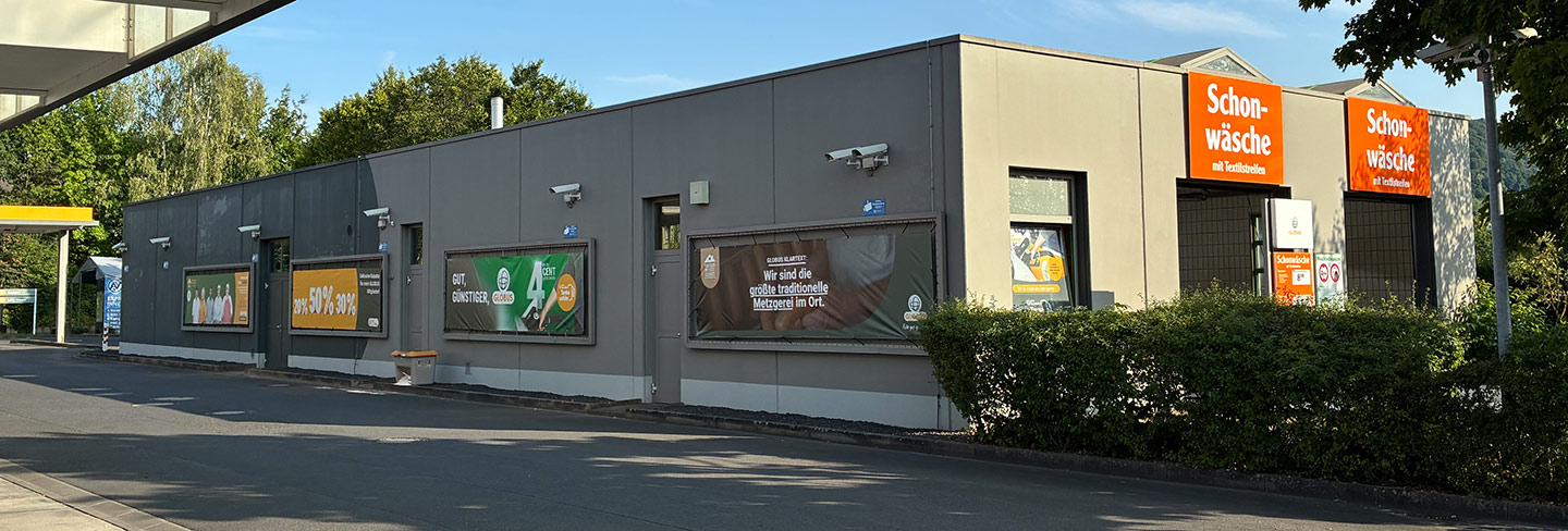 Das Gebäude zeigt Werbeplakate von GLOBUS, darunter Angebote und den Hinweis auf eine traditionelle Metzgerei im Ort.