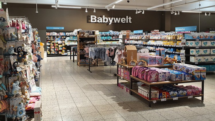 Regalreihen mit Babyartikeln, Spielzeug, Kleidung und Pflegeprodukten in einem Bereich mit dem Schriftzug Babywelt an der Wand.