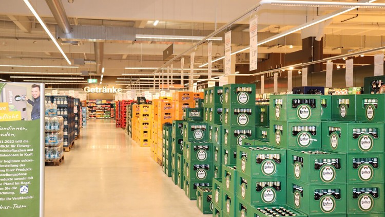 Mehrere Bierkästen und Getränkekisten in grüner, gelber und orangefarbener Verpackung stehen im Getränkebereich eines Marktes.