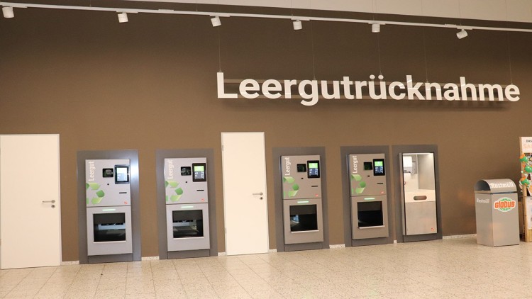 Sechs Automaten zur Leergutrücknahme, Beschriftung „Leergutrücknahme“ an brauner Wand, rechts daneben ein Restmüllbehälter.