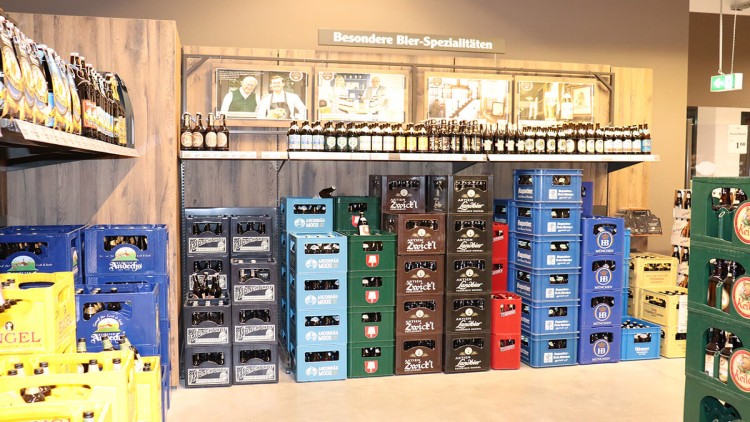 Regale und Stapel mit Bierkisten verschiedener Marken, darüber ein Schild mit der Aufschrift Besondere Bier-Spezialitäten.