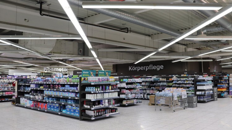 Regale mit Kosmetik- und Körperpflegeprodukten, Beschriftung „Kosmetik“ und „Körperpflege“, helle Beleuchtung, Industriedecke.