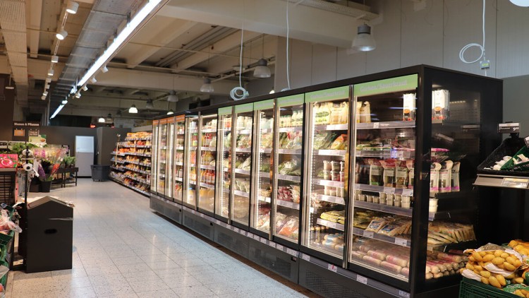 Eine Reihe von beleuchteten Kühlregalen mit Lebensmitteln wie Joghurt, Getränken und Gemüse im GLOBUS Markt.