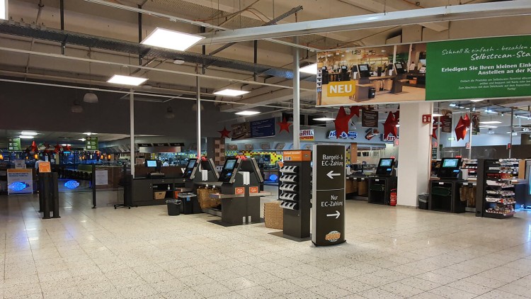 Selbstscan-Kassen im GLOBUS-Markt mit Hinweisschildern für Bar- und EC-Zahlung sowie Dekoration mit roten Sternen.