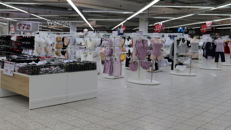 Verkaufsfläche mit Damenunterwäsche, Schlafkleidung und Socken auf Ständern und in Körben, darüber Schild mit Schriftzug \