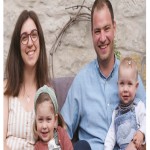 Zwei Erwachsene und zwei Kinder sitzen auf einem Sofa vor einer Steinwand, eines der Kinder trägt eine Kopfbedeckung.